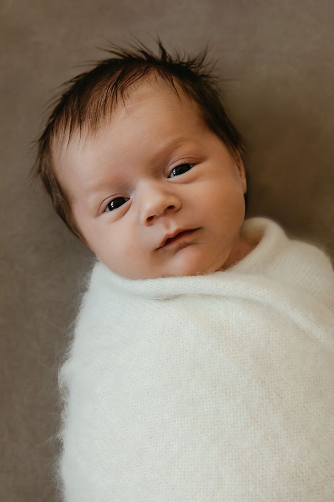photo of a newborn wrapped in a swaddle looking wide-eyed at the camera at a newborn session on Cape Cod