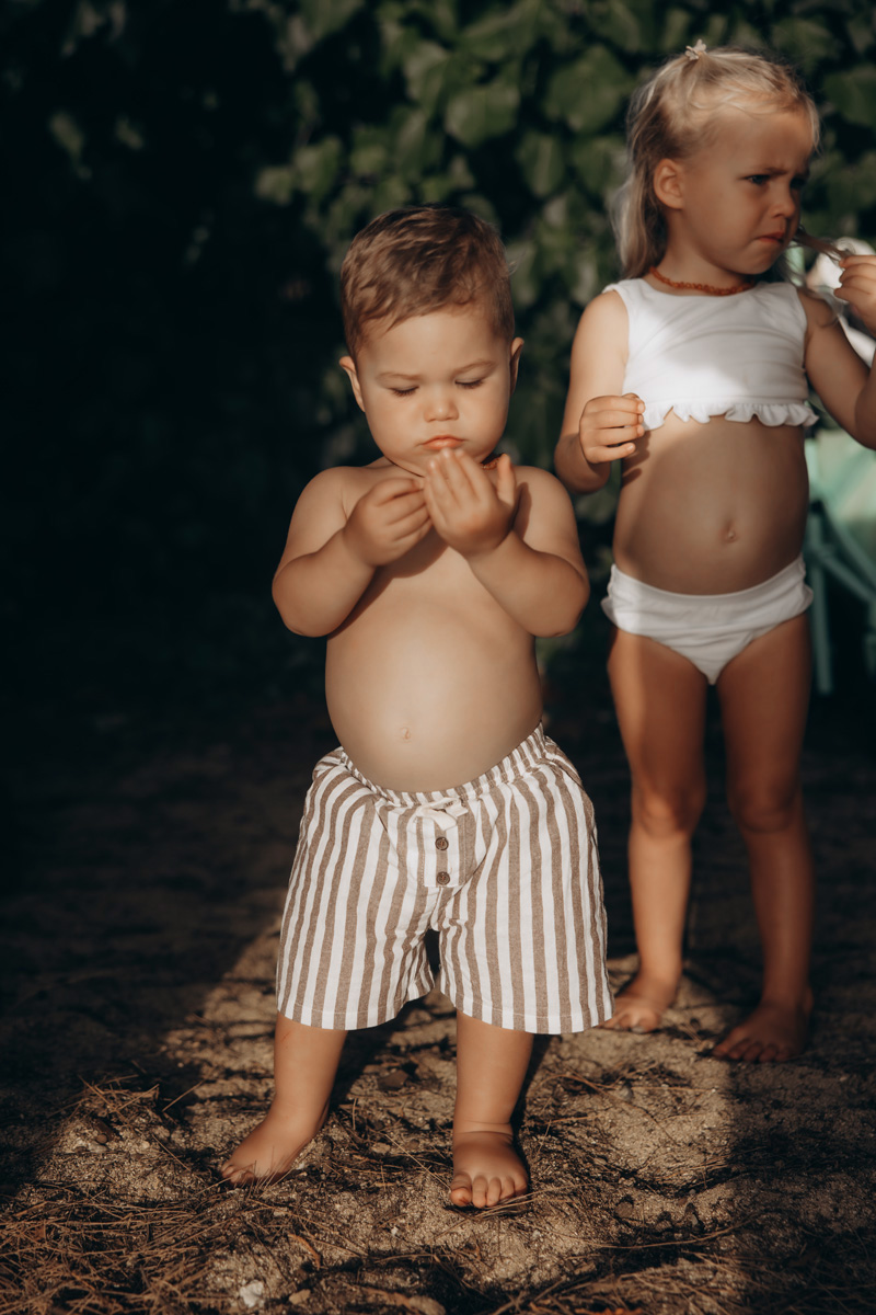 Little boy in a striped swimsuit looking at something in his hand in a bush cove by Cape Cod Photographer Caryn Scanlan