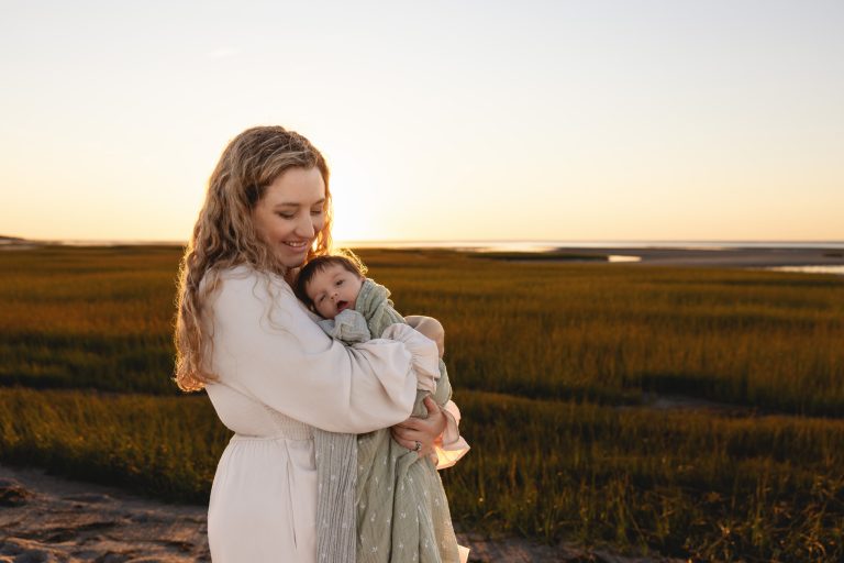 brewster newborn photographer caryn Scanlan's photo of a mother cradling her newborn on a beach in front of grassy tide pools