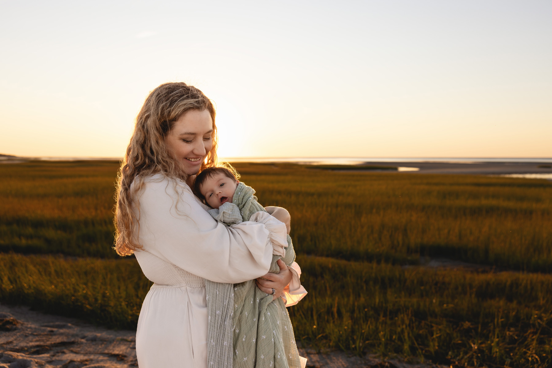 brewster newborn photographer caryn Scanlan's photo of a mother cradling her newborn on a beach in front of grassy tide pools