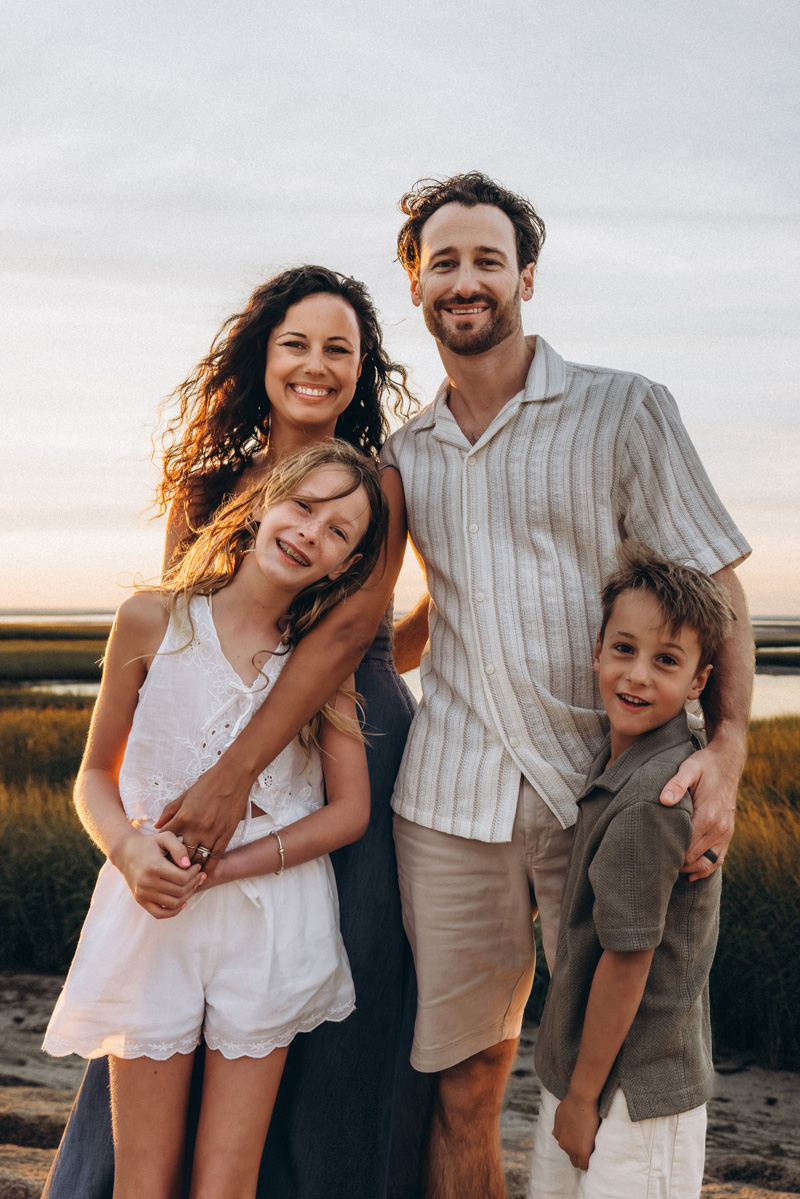 Family standing happily together in front of some grassy tide pools on the beach by Cape Cod Family Photographer Caryn Scanlan
