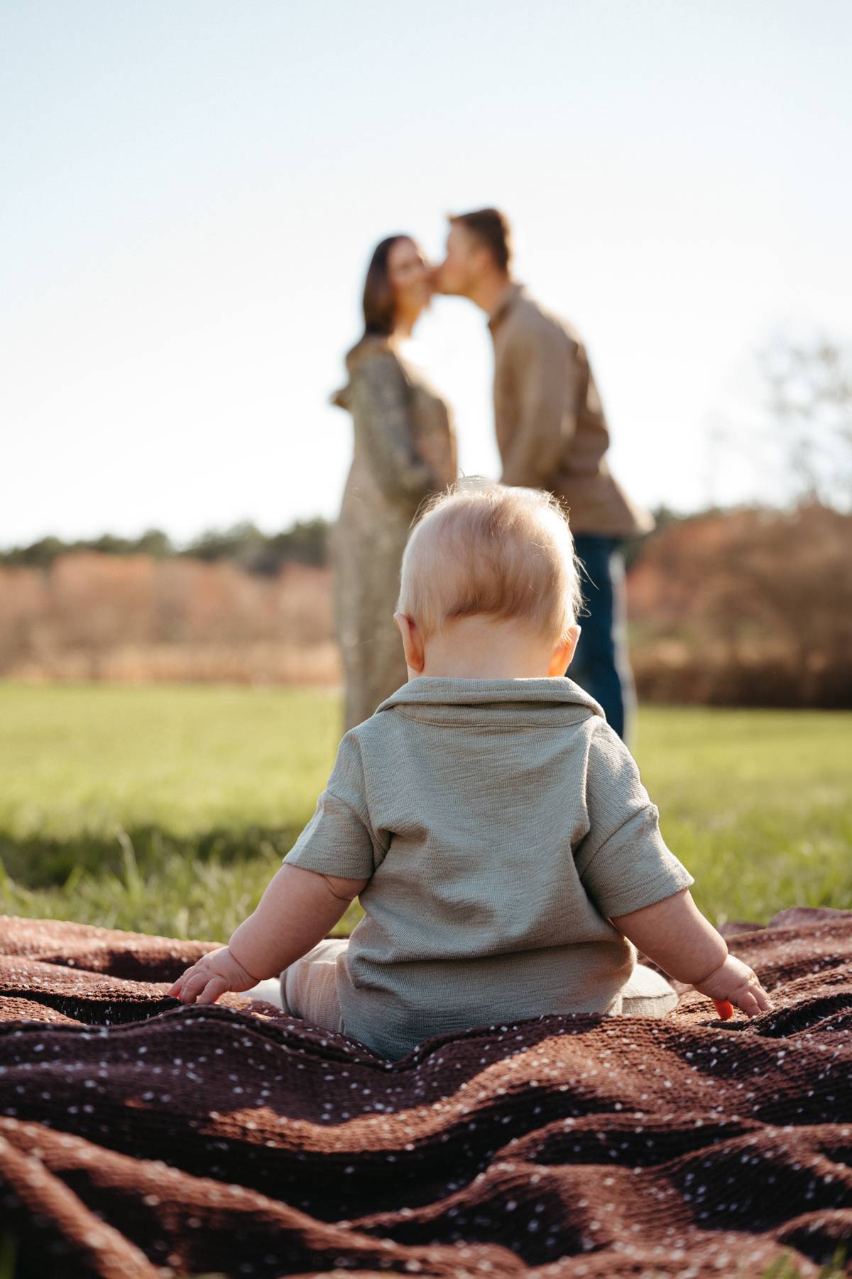 6 month old baby session on the South Shore MA sitting with his parents in the distance