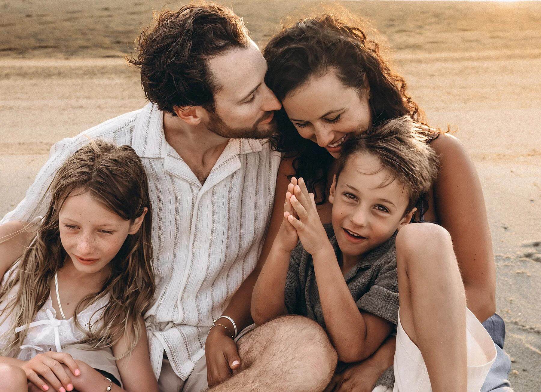 Cape Cod Family & Maternity Photographer 9 Cape Cod Family session photo of a family sitting close together on the beach, with the day nuzzling into his wife in a sweet, cosy moment